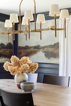 a dining room table with a vase on top of it and four lights hanging from the ceiling