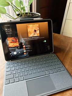 an open laptop computer sitting on top of a wooden table next to a potted plant