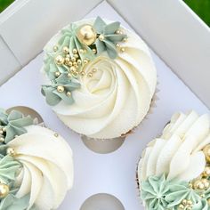 three cupcakes with white frosting and green decorations on them in a box