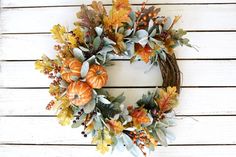 a wreath is hanging on the side of a white wall with autumn leaves and pumpkins