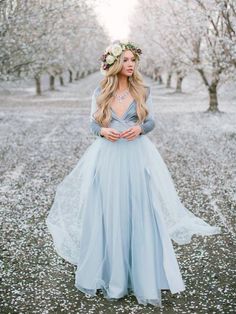 a woman wearing a blue dress standing in the middle of an almond tree filled field