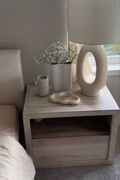 a white vase with flowers on top of a table next to a lamp and chair