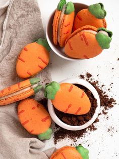 three little carrots are sitting in small white bowls with dirt on the ground next to them