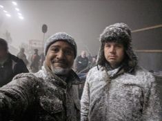 two men standing next to each other in front of a crowd on a snowy day