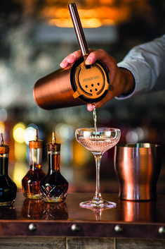 a bartender is pouring a drink into a wine glass with two liquor bottles in the background