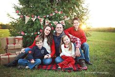 a family sitting in front of a christmas tree with presents on the grass under it