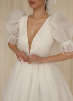 a woman in a white wedding dress with pearls on her head and hands behind her back