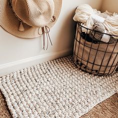 a basket and hat on the floor next to a wall with a rug in it