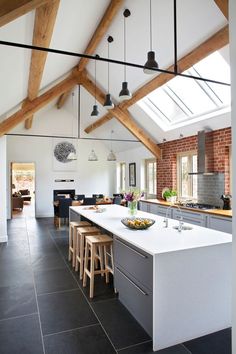 an open kitchen and dining room area with exposed beams in the ceiling, white counter tops and black tile flooring