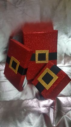 three red boxes with gold and black designs on them sitting on a silver cloth covered surface