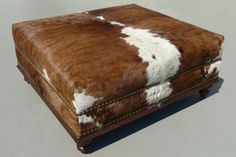 a brown and white cow hide ottoman with studded trimmings on the sides