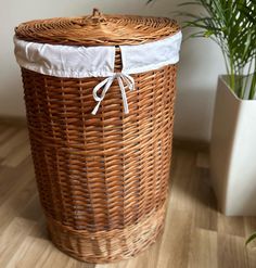 a wicker laundry basket with white lining on the bottom, and a potted plant in the background