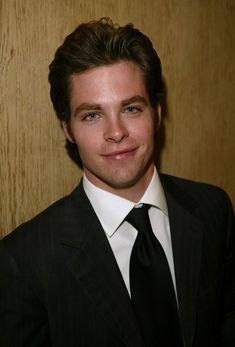 a young man in a suit and tie posing for a photo against a wooden wall