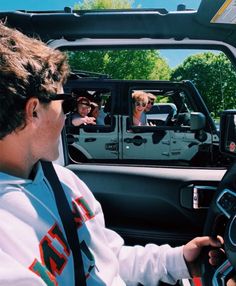 a man driving a jeep with two women in the back seat and one woman behind the steering wheel