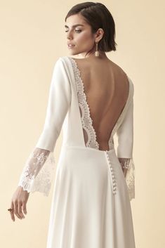 the back of a woman wearing a white dress with long sleeves and lace on it