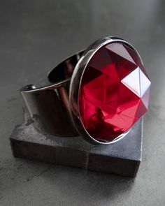 Unveil your dark side this Halloween with the 'VAMPIRE'S KISS' ring. Featuring a bold vintage cabochon in a deep, blood-red hue, this ring captures the essence of mystery and dark romance. Set in a black gunmetal band, the large crystal-like faceted glass cabochon evokes the glamour of gothic royalty. Whether you're casting spells or simply reveling in the night, this piece adds just the right amount of eerie elegance. The VAMPIRE'S KISS ring will have you dripping with dark allure--add a little sexy-sinister sophistication to your Halloween or everyday goth wardrobe! Gift this ring to the gothic alt girl in your life, or keep it as your signature statement as you celebrate the season of shadows.  DETAILS: - Vintage faceted glass cabochon: 18mm (3/4") dia - Black gunmetal plated ring base Gothic Royalty, Goth Wardrobe, Everyday Goth, Vampire Kiss, Teen Halloween, Casting Spells, Red Ring, Red Rings, Gothic Halloween