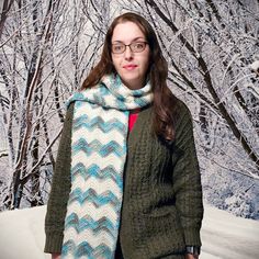 a woman standing in the snow wearing a knitted scarf and sweater over her shoulders