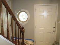 an entry way with a round window and white painted door, next to a stair case