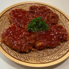 two pieces of meat covered in sauce on a brown and white plate with a sprig of parsley