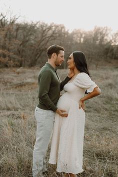 a pregnant woman standing next to a man in a field