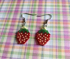 a pair of red and green beaded strawberry earrings on a plaid tablecloth background