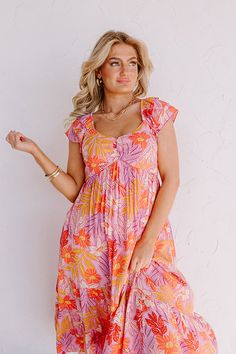 - Enjoy a laid back day in the sun in this darling dress! - Material with an orange, pink, and purple hued botanical print - A built-in lining ending mid-thigh - An elastic scoop neckline - Short flutter sleeves - A smocked upper back - Hidden side pockets - A flowy yet flattering silhouette that ends in a midi length hemline Back Day, Darling Dress, Purple Hues, Botanical Print, Dress Material, Pink And Purple, Flutter Sleeves, Orange Pink, Botanical Prints