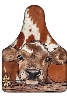 a brown and white cow laying down next to a wooden board with a flower in it's mouth