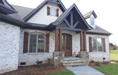 a white brick house with brown shutters on the front door and windows, along with stone steps leading up to it