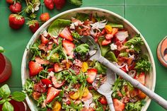 a salad with strawberries and other vegetables on a green table next to some drinks