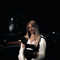 a woman with long blonde hair is sitting in a car and holding a black object