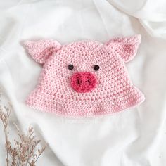 a pink crocheted pig hat laying on top of a white sheet with flowers