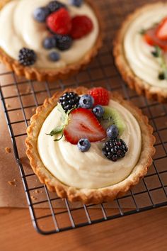 three small desserts on a cooling rack with berries and kiwi in the middle