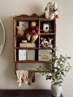 a wooden shelf with books and stuffed animals on it next to a potted plant