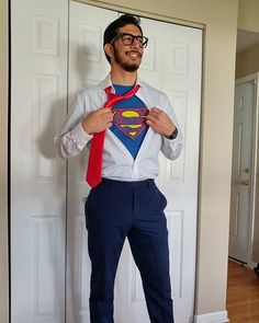 a man wearing a superman shirt and tie standing in front of a door with his hands on his hips