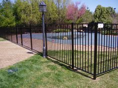 a black iron fence in front of a pond with a lamp post on the side