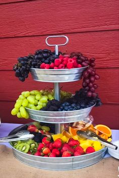 three tiered trays filled with fruit on top of a wooden table next to a red wall