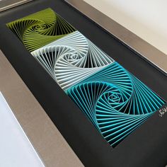 three different colored paper art pieces in a black frame on a white table with silver trim