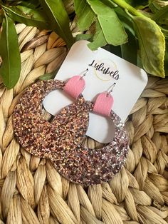 the pink and gold earrings are on top of a woven basket next to a plant