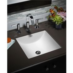 a white sink sitting on top of a black counter next to a vase with flowers