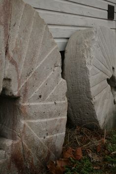 two large rocks sitting next to each other in front of a white wall and grass