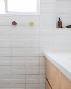 a white tiled bathroom with wooden cabinets and countertop space, along with a window above the sink