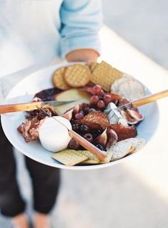 a person holding a white bowl filled with food and crackers on top of it