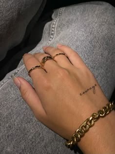 a woman's hand with two gold rings on her left and the word courage written in cursive writing