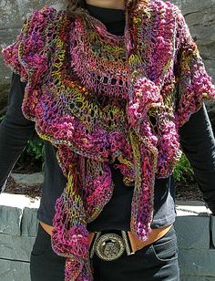 a woman is wearing a colorful knitted shawl and black t - shirt while standing in front of a stone wall