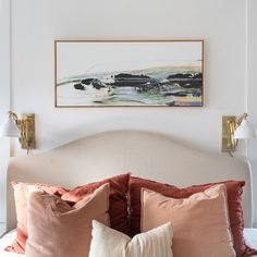 a bed with two pillows on top of it and a painting above the headboard