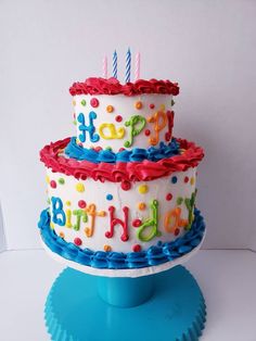 a three tiered birthday cake with candles on it's top and the words happy birthday written in multi - colored icing