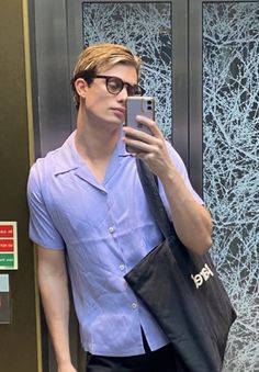 a man with glasses is looking at his cell phone while standing in front of an elevator