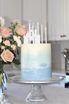 a blue and white cake sitting on top of a table next to pink flowers in vases