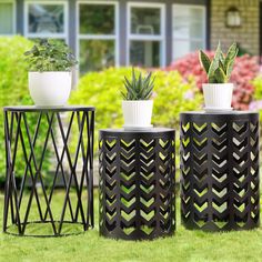 three black planters sitting on top of green grass next to plants in white vases