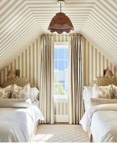 two beds in a room with striped walls and curtains on the windowsill, one has a chandelier hanging from the ceiling